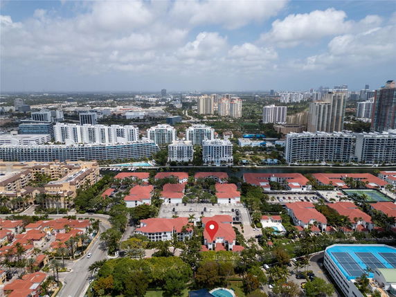 Aerial view of a residential area with multiple buildings and red roofs, surrounded by taller commercial and residential structures.