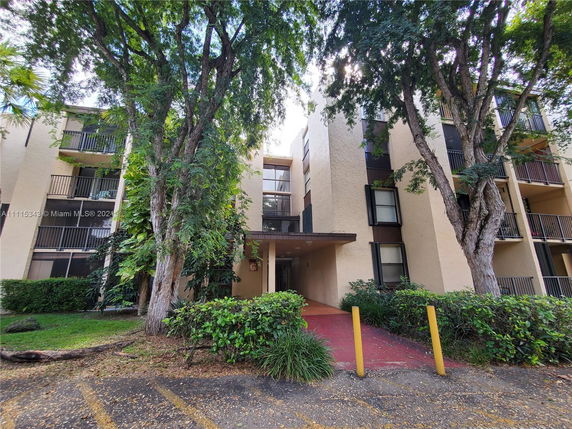 Front view of a multi-story apartment building with balconies and trees in front.