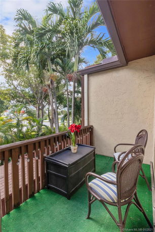Balcony area with chairs and a small table overlooking palm trees.