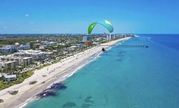 Wide angle view of a coastline with buildings and a paraglider over the ocean.