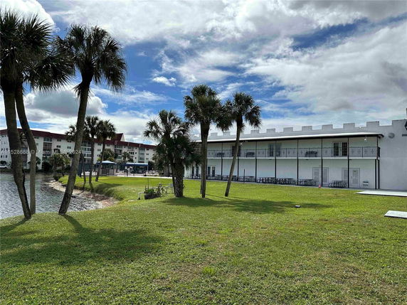 View of a two-story building with balconies, near a water body and surrounded by palm trees.
