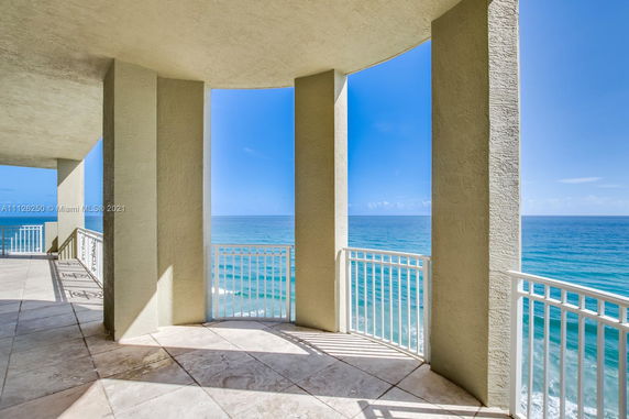 View from a balcony overlooking the ocean with blue skies and white railing.