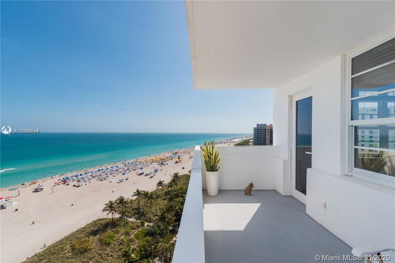 View from a building balcony overlooking a sandy beach and ocean with blue and yellow umbrellas.