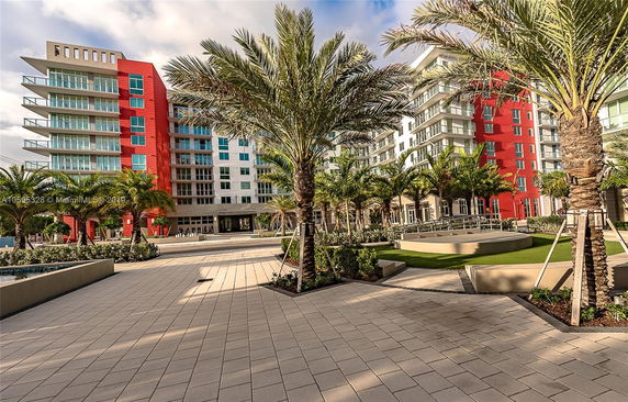 Front view of a multi-story building with red and white exterior, featuring balconies and surrounded by palm trees.