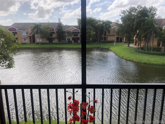 View from a balcony overlooking a pond with buildings and trees in the background.