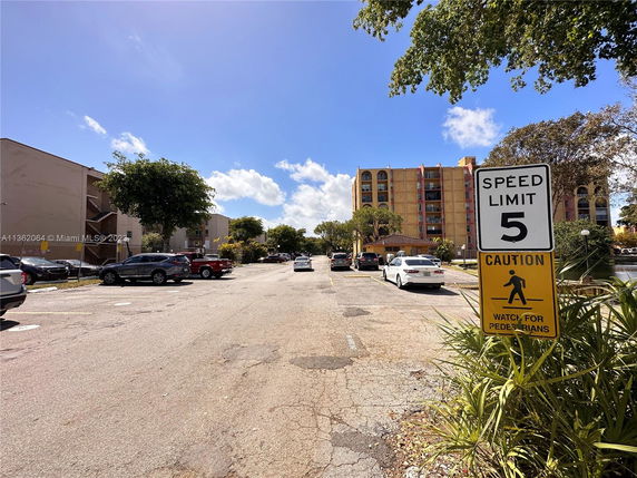 Outdoor parking area with several parked cars and buildings in the background.