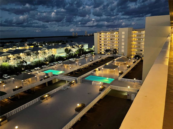 Wide angle view of a building complex at night with illuminated parking and swimming pool.