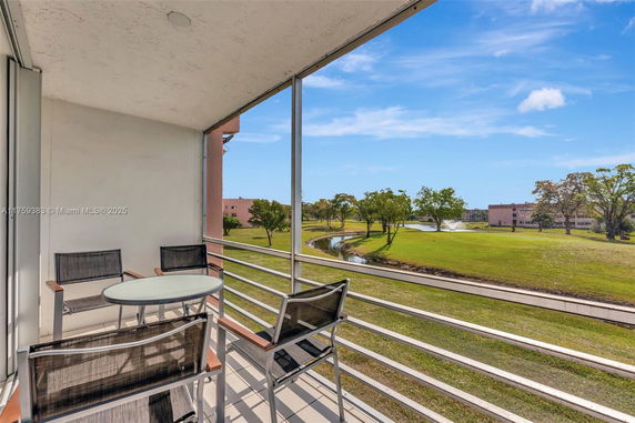 Balcony with table and chairs overlooking a grassy area with trees and a water feature.
