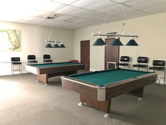 Indoor room with two billiard tables and chairs.