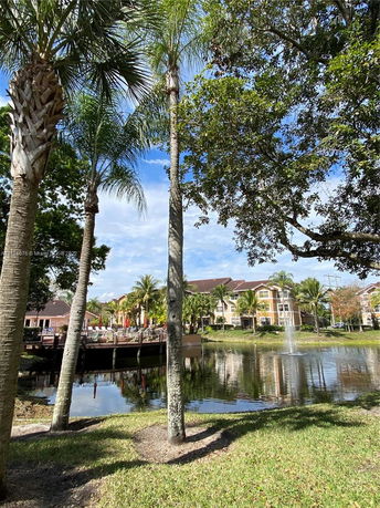 View of multi-story buildings with balconies and a water feature surrounded by trees.