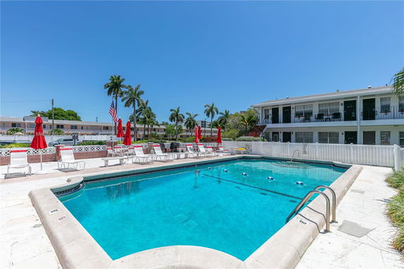 Outdoor swimming pool with surrounding chairs and umbrellas in front of a two-story building.
