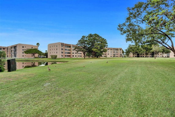 View of a grassy area with a pond, surrounded by multi-story residential buildings.
