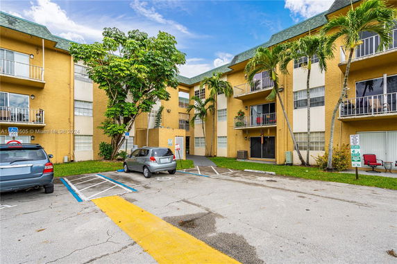 Front view of a three-story apartment building with balconies and parking space.