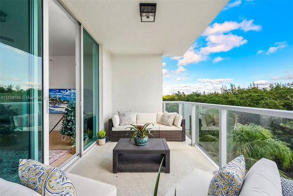 Balcony with outdoor seating area and glass railing overlooking green surroundings.