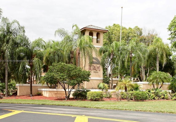Front view of a building entrance with palm trees and a sign reading 'The Palms.'