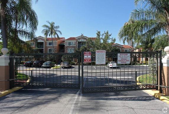 Front view of a multi-story residential building with gated entrance and parking area.