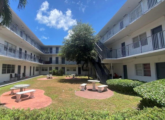 Courtyard view of a three-story apartment building with balconies and a central lawn area with benches.