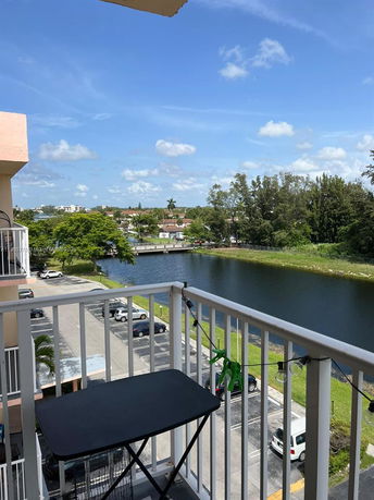 Panoramic view from a balcony overlooking a parking area and a small body of water with surrounding greenery.
