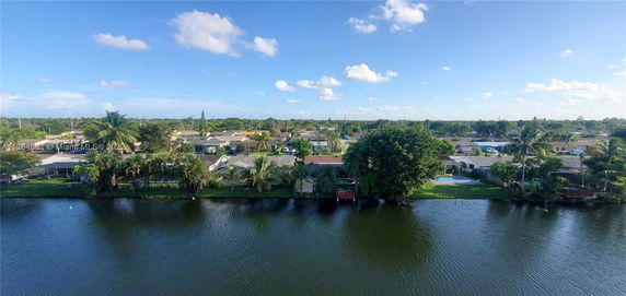 Panoramic view of a residential area with houses, trees, and a body of water in the foreground.