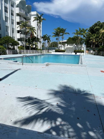 View of a swimming pool area near a residential building with palm trees around.