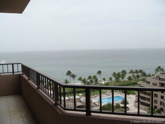 Balcony view overlooking the ocean and a distant swimming pool.