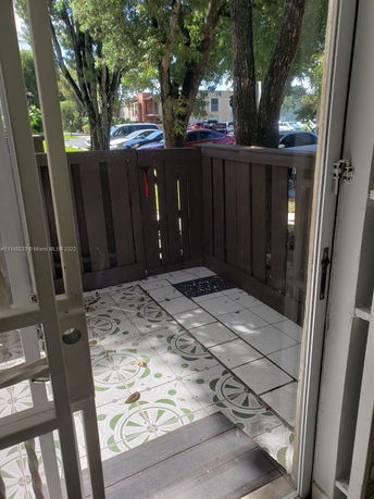 View from a patio with tiled floor and wooden fence, overlooking parked cars and trees.