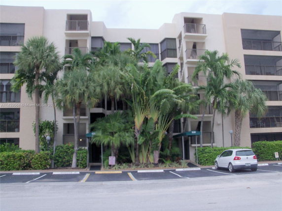 Front view of a multi-unit apartment building with balconies and palm trees in front.