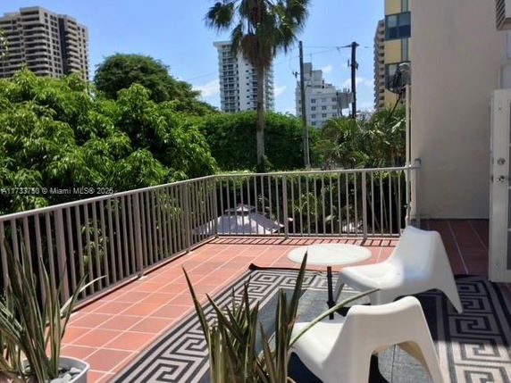Balcony with chairs and potted plants overlooking surrounding buildings and greenery.