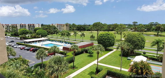 View of multiple residential buildings surrounded by green lawns, trees, and a pool area.