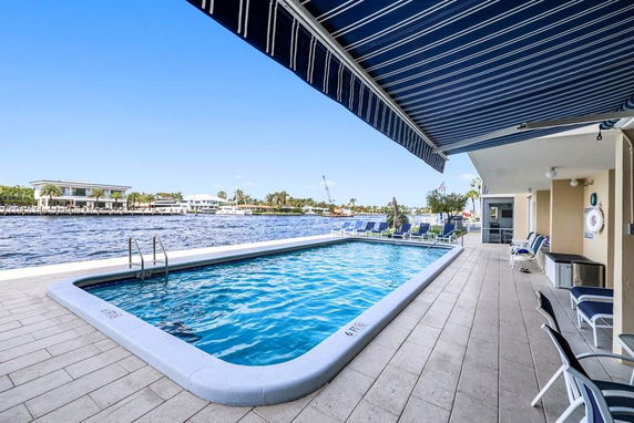 Outdoor swimming pool area with lounge chairs next to a waterway.