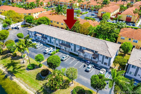 Aerial view of a residential building with adjacent parking area and cars.