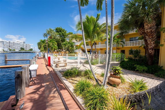 Outdoor area with a swimming pool surrounded by a fence, palm trees, and a waterfront walkway.