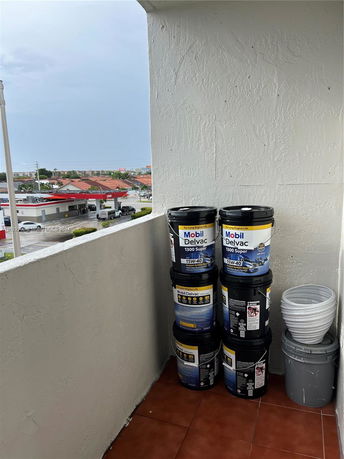 Outdoor area with buckets stacked on a balcony overlooking a gas station and other buildings.