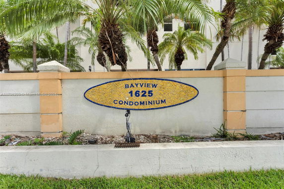 Front view of a condominium sign on a stone wall with palm trees in the background.