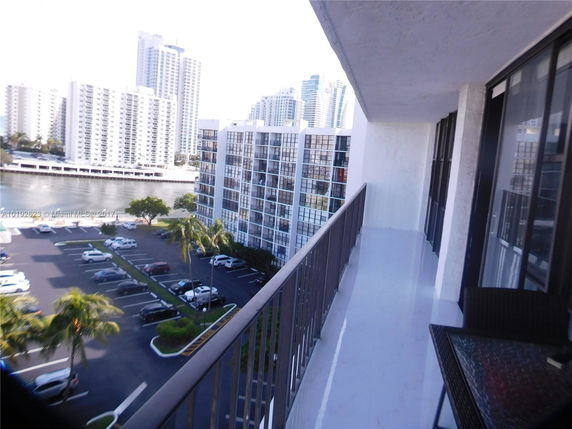 View from a balcony overlooking a parking area and adjacent high-rise buildings.