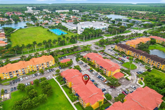 Aerial view of residential area with multiple buildings and parking spaces, surrounded by greenery and roads.