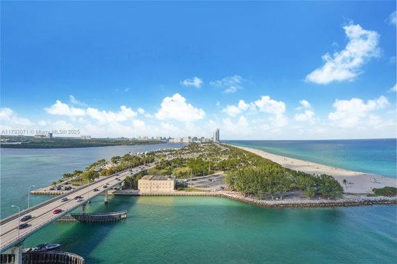 Panoramic view of a coastal area with a bridge and beach, showing clear blue skies and ocean waters.