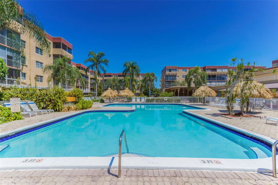 A swimming pool area surrounded by multi-story buildings and palm trees.