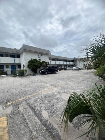 Outdoor parking area in front of a two-story building with a grey roof and white walls.