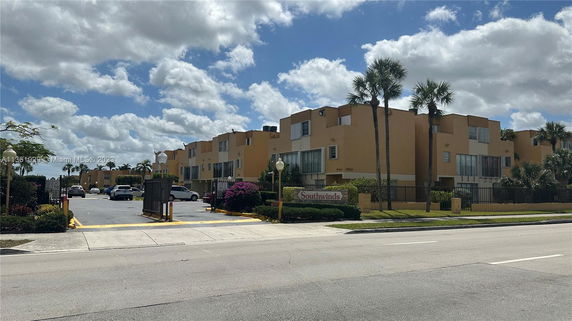 Front view of a multi-story apartment complex with gated entrance and parking area.