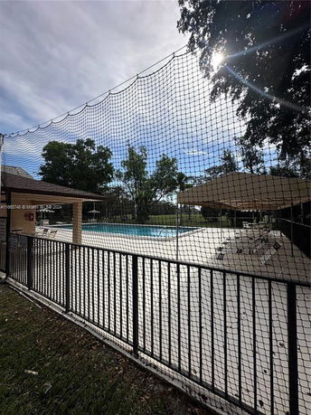 Outdoor view of a swimming pool with surrounding fence and lounge chairs.