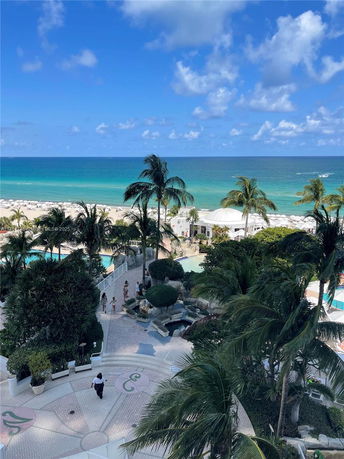 Panoramic view of the beach and ocean from a high vantage point with palm trees and a walkway.