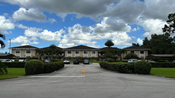 Front view of a large multi-unit residential building with a parking area.
