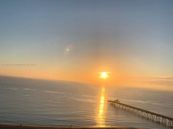 Panoramic view of the ocean with a pier extending into the water and the sun setting in the background.