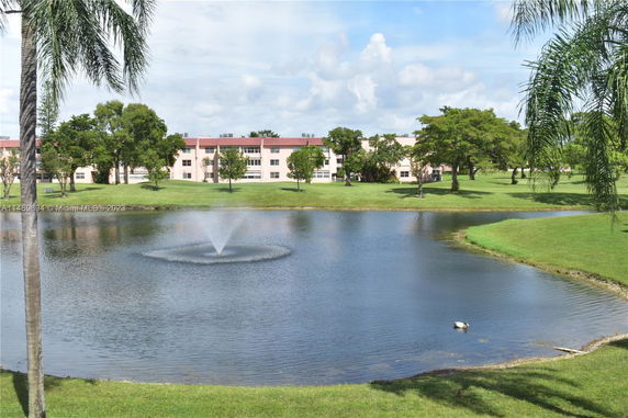 View of a lake with a fountain and a residential building in the background.