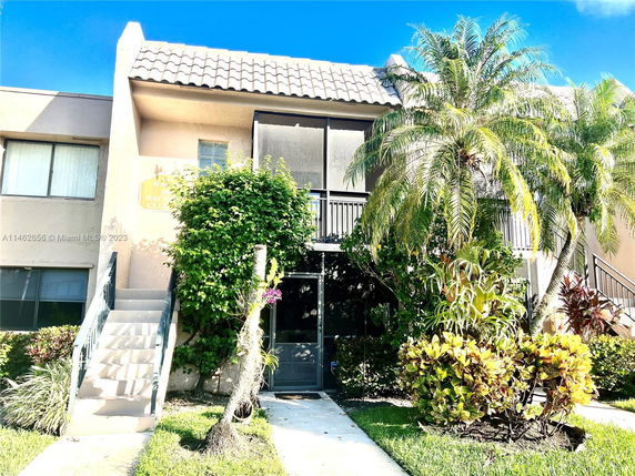 Front view of a two-story building with exterior stairs and tropical landscaping.