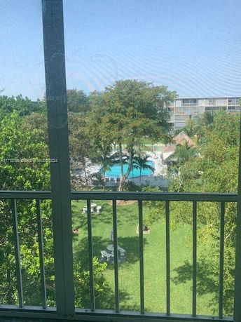 View from a building overlooking a swimming pool and landscaped area with trees.