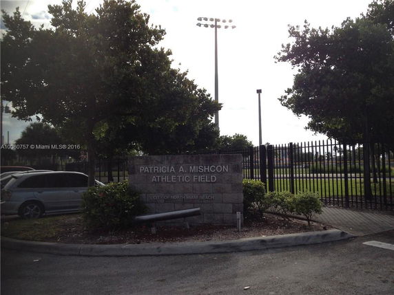 Entrance sign for Patricia A. Mishcon Athletic Field surrounded by trees and a metal fence.