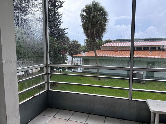 View from a covered porch showing a building with a metal roof and surrounding trees.