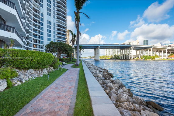 View of a waterfront area with a high-rise building and a bridge in the background.